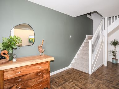 A hallway with a wooden dresser and a large mirror on the wall stairs with white railing and carpeted steps and a potted plant at Y Goedwig in Newborough