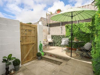 An outdoor patio area with a wooden gate potted plants a green umbrella table and chairs at Y Goedwig in Newborough