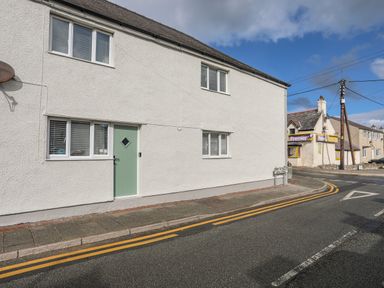 A white building with a green door and windows on a street corner near a Premier store at Y Goedwig in Newborough