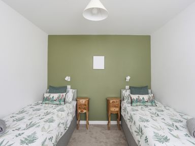 A bedroom with two single beds a green accent wall and wooden bedside tables at Y Goedwig in Newborough