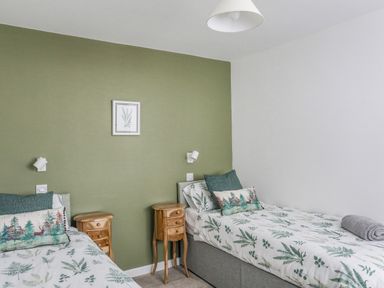 A bedroom with two single beds green accent wall and wooden bedside tables at Y Goedwig in Newborough