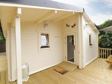 An exterior view of a small building with wooden decking a door two windows wall lamps and decorative butterflies at Port Heron Lodge Ballykeeran near Glasson County Westmeath