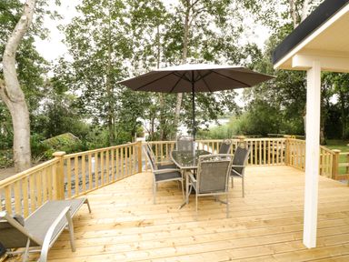 An outdoor wooden deck with a glass table and six chairs under a large umbrella near trees at Port Heron Lodge Ballykeeran near Glasson County Westmeath