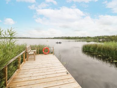 A wooden dock with a bench and a lifebuoy overlooking a lake with two people canoeing at Port Heron Lodge in Ballykeeran near Glasson County Westmeath