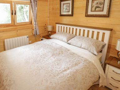 A bedroom with a bed and patterned bedding beside wooden walls with framed pictures at Port Heron Lodge in Ballykeeran near Glasson County Westmeath