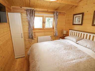 A bedroom with a double bed bedside table with lamp wardrobe and window with curtains at Port Heron Lodge Ballykeeran near Glasson County Westmeath