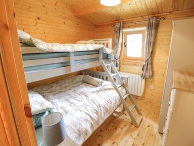 A small wooden bedroom with bunk beds a window with curtains a wardrobe and a lamp at Port Heron Lodge Ballykeeran near Glasson County Westmeath