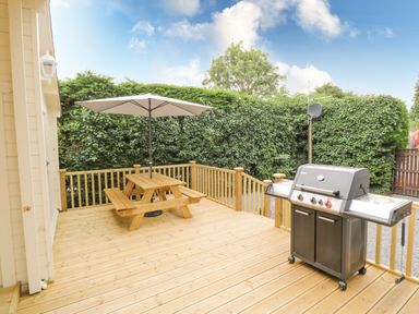 A wooden outdoor deck with a picnic table and umbrella and a gas grill in a backyard at Port Heron Lodge in Ballykeeran near Glasson County Westmeath