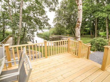 A wooden deck with metal chairs overlooking a river and surrounded by trees at Port Heron Lodge in Ballykeeran near Glasson County Westmeath