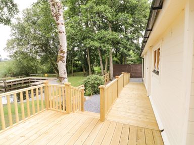 A wooden deck with railings attached to a beige building near a lake and surrounded by trees at Port Heron Lodge Ballykeeran near Glasson County Westmeath