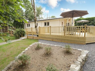 An outdoor deck with umbrellas and tables around a white building with surrounding trees and a small garden bed at Port Heron Lodge Ballykeeran near Glasson County Westmeath