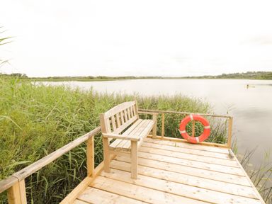 A wooden bench on a dock by a lake with tall grass and a life ring at Port Heron Lodge in Ballykeeran near Glasson County Westmeath