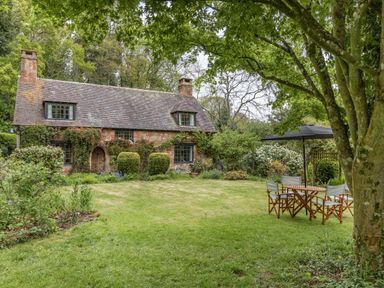 A stone cottage with a garden lawn and outdoor table with chairs under a tree at Saint Pancras Chapel in Washford near Williton