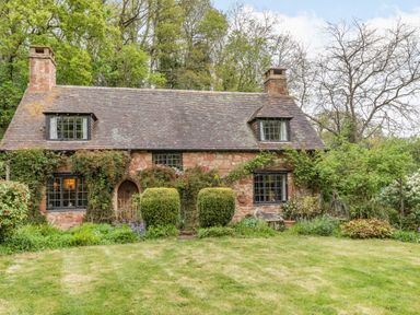 A stone cottage with a tiled roof two chimneys and trimmed bushes in front at Saint Pancras Chapel in Washford near Williton