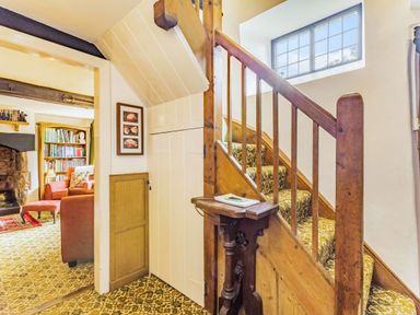 A staircase with patterned carpet and wooden railing next to a hallway with a closed door leading to a living room with bookshelves and armchairs at Saint Pancras Chapel in Washford near Williton