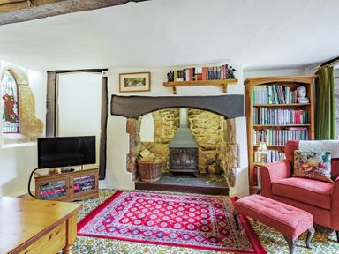 A living room with a wood stove fireplace a red armchair a red patterned rug a wooden bookshelf and a television at Saint Pancras Chapel in Washford near Williton