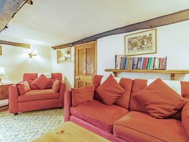 A sitting room with red sofas a wooden door books on a shelf and framed pictures on the wall at Saint Pancras Chapel in Washford near Williton