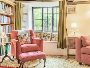 A sitting room with a pink armchair footstool bookshelf and window seat at Saint Pancras Chapel in Washford near Williton