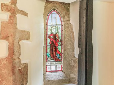 A stained glass window with a religious figure in a stone wall at Saint Pancras Chapel in Washford near Williton