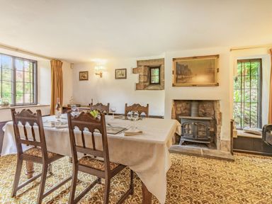 A dining room with a table covered by a tablecloth surrounded by wooden chairs a wood stove fireplace and windows at Saint Pancras Chapel in Washford near Williton
