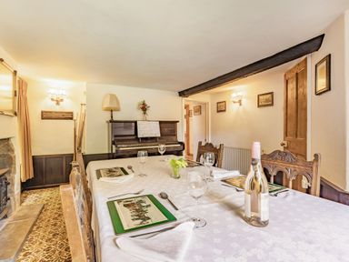 A dining room with a table set with plates wine glasses and a bottle in front of a piano at Saint Pancras Chapel in Washford near Williton