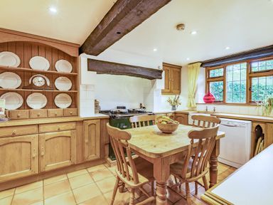 A kitchen with wooden cabinets a dining table with chairs and a bowl of fruit at Saint Pancras Chapel in Washford near Williton