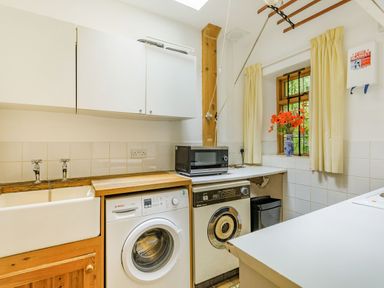 A laundry room with a washing machine dryer sink cabinets microwave and a window with flowers at Saint Pancras Chapel in Washford near Williton