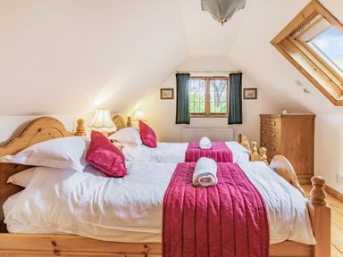 A bedroom with two single beds white linens red bed runners and pillows wooden furniture and window with green curtains at Saint Pancras Chapel in Washford near Williton