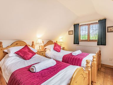 A bedroom with two single beds with red bedding and pillows wooden cupboards and a window with curtains at Saint Pancras Chapel in Washford near Williton