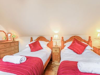 A bedroom with two single wooden beds with red pillows and blankets and wooden furniture with lamps at Saint Pancras Chapel in Washford near Williton