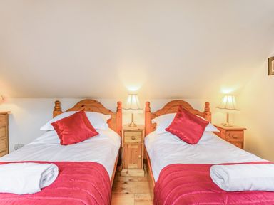 A bedroom with two single beds with red pillows and blankets a bedside table with a lamp and wooden furniture at Saint Pancras Chapel in Washford near Williton
