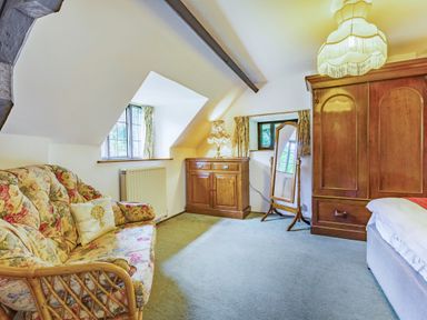 A bedroom with a floral sofa wooden wardrobe standing mirror and wooden cabinet at Saint Pancras Chapel in Washford near Williton