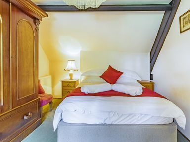 A bedroom with a bed with white and red bedding two rolled towels a wooden wardrobe two bedside tables a lamp and a red chair at Saint Pancras Chapel in Washford near Williton