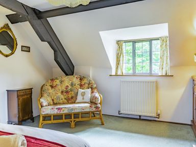 A bedroom corner with a floral loveseat wooden cabinet window and radiator at Saint Pancras Chapel in Washford near Williton