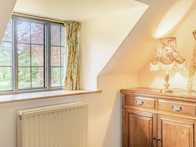 A window with floral curtains and a wooden cabinet with a lamp in a room at Saint Pancras Chapel in Washford near Williton