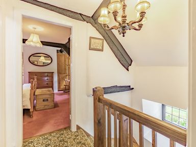 A hallway with wooden railing and patterned carpet leading to a bedroom with wooden furniture at Saint Pancras Chapel in Washford near Williton