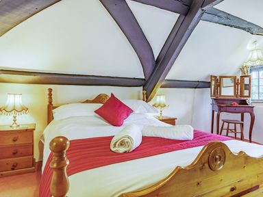 A bedroom with a wooden bed a red cushion two bedside tables lamps and a dressing table at Saint Pancras Chapel in Washford near Williton