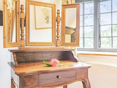 A wooden dressing table with three mirrors and a pink flower on top by a window at Saint Pancras Chapel in Washford near Williton