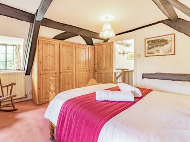 A bedroom with a wooden bed with white linens and red throw a wooden wardrobe a wooden rocking chair and ceiling beams at Saint Pancras Chapel in Washford near Williton