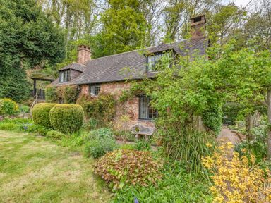 A stone cottage with a slate roof surrounded by a garden with bushes and trees at Saint Pancras Chapel in Washford near Williton