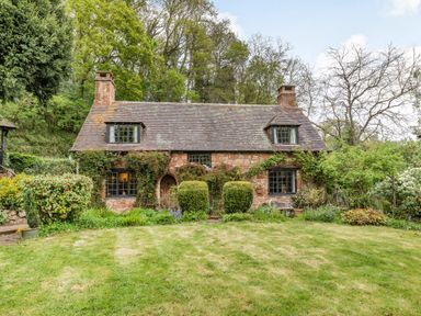 A stone cottage with a tiled roof surrounded by trees and bushes at Saint Pancras Chapel in Washford near Williton