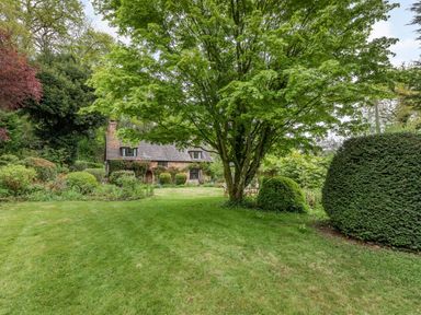 A garden with a large tree and trimmed hedges in front of a brick house at Saint Pancras Chapel in Washford near Williton
