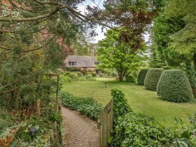 A pathway leading through a garden with trimmed bushes and a house in the background at Saint Pancras Chapel in Washford near Williton