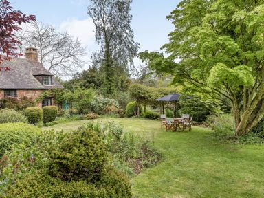 A garden with trimmed bushes a large tree and outdoor table with chairs and umbrella at Saint Pancras Chapel in Washford near Williton