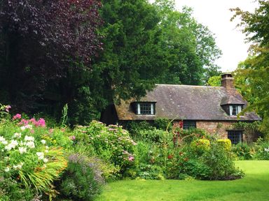 A stone cottage with a slate roof surrounded by a garden with flowers and trees at Saint Pancras Chapel in Washford near Williton