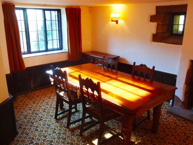 A dining room with wooden table and chairs near a window with orange curtains at Saint Pancras Chapel in Washford near Williton