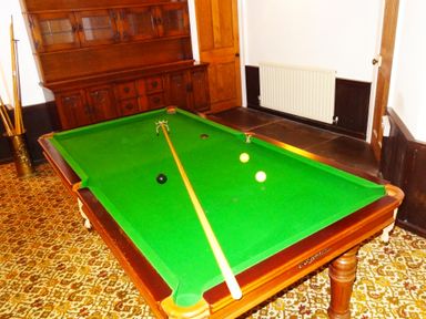 A room with a green snooker table several balls and a cue stick a wooden cabinet a door and patterned carpet at Saint Pancras Chapel in Washford near Williton