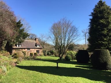 A grassy garden with trimmed bushes and a stone cottage at Saint Pancras Chapel in Washford near Williton