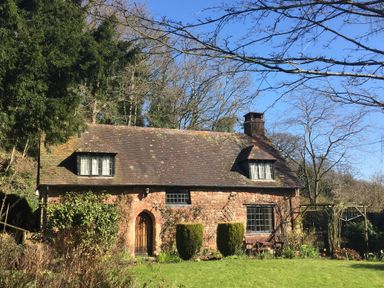 A stone cottage with a tiled roof and wooden door surrounded by trees and garden at Saint Pancras Chapel in Washford near Williton