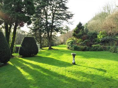A garden with trimmed trees green grass and a sundial at Saint Pancras Chapel in Washford near Williton